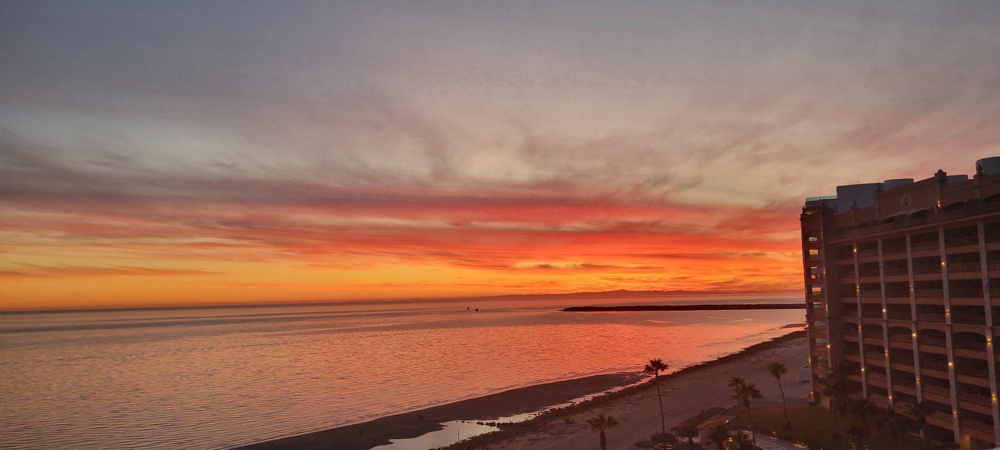 Vivid orange sunset reflected across calm water beside the resort