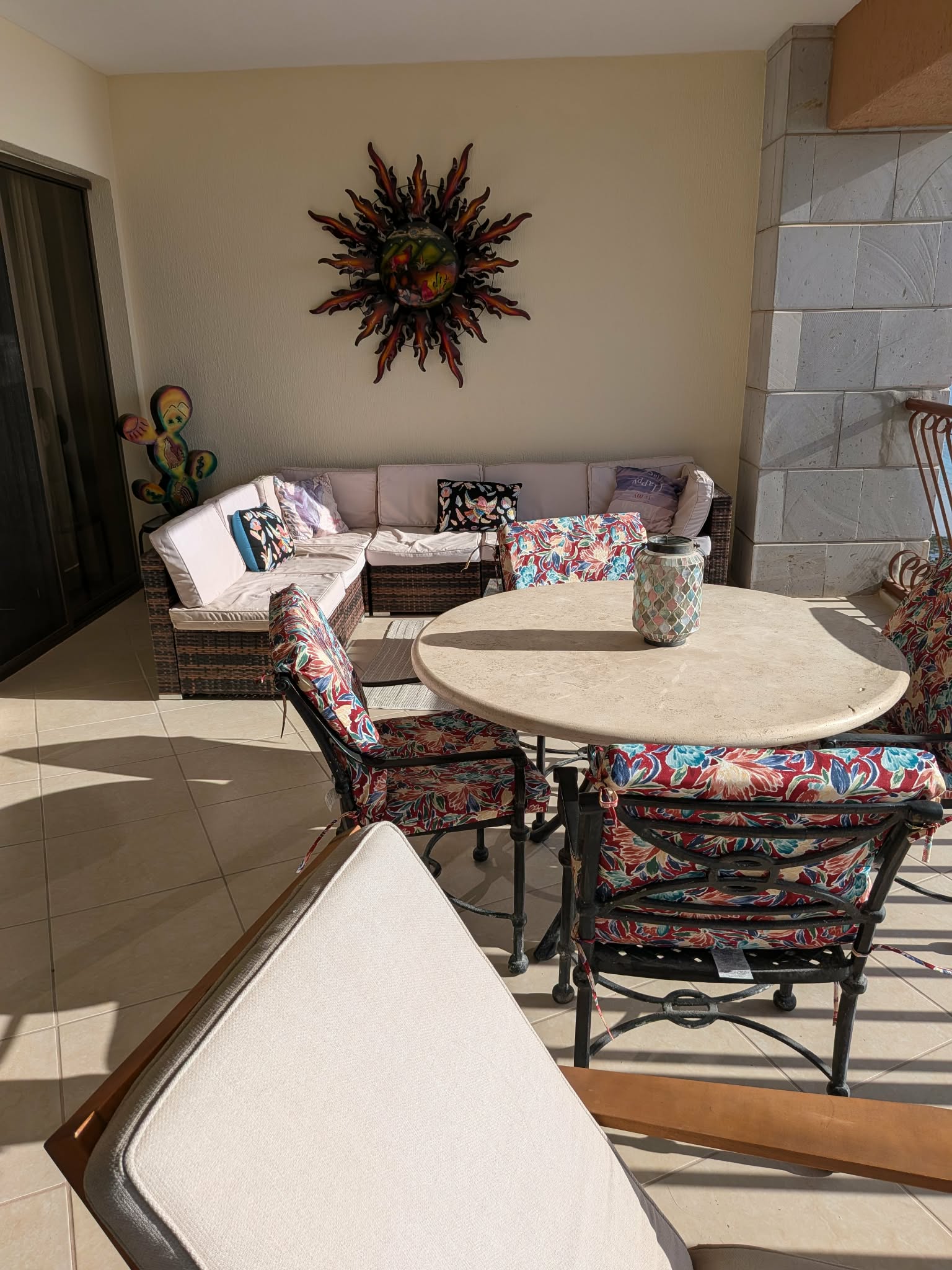 Balcony lounge seating and a round dining table beneath colorful sun wall art